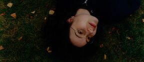 Person in glasses lying on green grass with autumn leaves, wearing a dark Aalto University hoodie