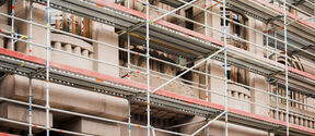 Metal scaffolding covers an ornate beige stone building with tall windows during renovation