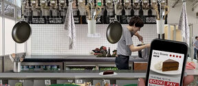 Modern kitchen with a cook, hanging pans and a phone showing a chocolate brownie review