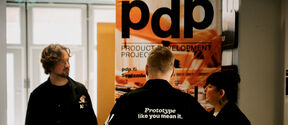 Aalto Design Factory’s three staff members stand in front of a Product Development Project banderol