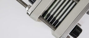 Close-up of a metal pasta machine showing cutting rollers and black adjustment knobs on a white background.