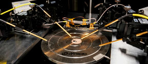 Close-up of a microchip wafer on a metal probe station with fine gold test needles around it