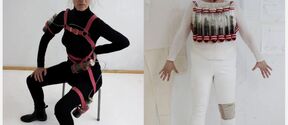 Two women pose in black and white outfits with strapped glass tubes worn as experimental body harnesses.