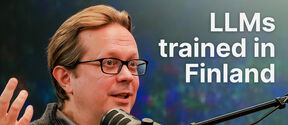 Man with glasses speaking into studio mic, text reads “LLMs trained in Finland” on colourful blurred background