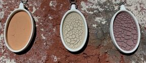 Three oval crackled pendants in white frames hang on thin chains against a rough brick wall.