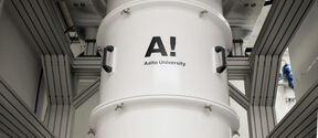 Large white cylindrical lab device in a metal frame, labelled Aalto University