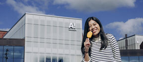 Smiling person holding yellow ice lolly outside modern glass building under blue sky