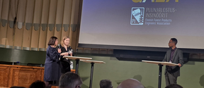 Three speakers at tall tables on a stage during the PI Scholarship Gala, facing an audience in a hall