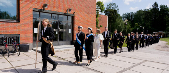 People walking in a procession next to a red brick building.