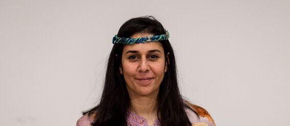 A person with black hair holding a certificate. They wear a purple floral dress with long sleeves.