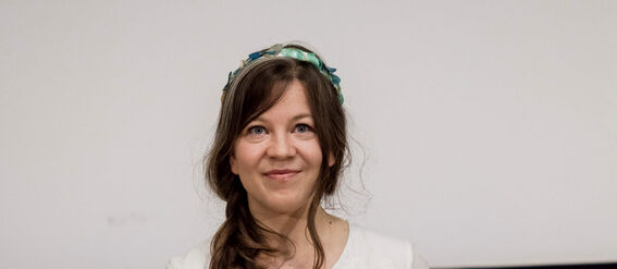Person in white dress holding certificate with doctoral hats in background