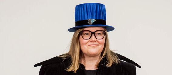 Person dressed in academic regalia holding a document. The hat is blue and the robe is black.