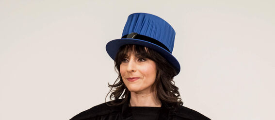 Person in academic robes and a blue doctoral hat holding a white diploma.
