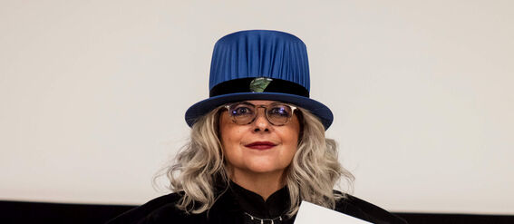 Person wearing black academic robes and blue hat, holding a diploma.