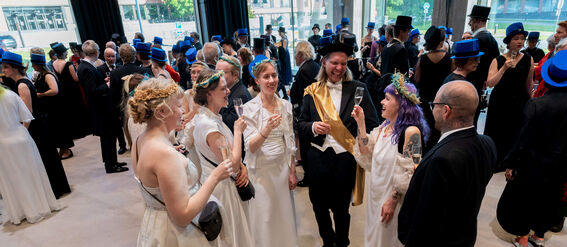 A formal gathering with people dressed in evening attire, including white gowns, floral headbands, and black suits.