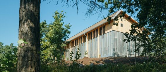 A modern wooden storage building with windows, surrounded by trees and greenery under a clear, blue sky.