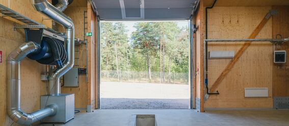 A storage with wooden walls and an open door, exposing trees outside. Metal ducts are visible inside.