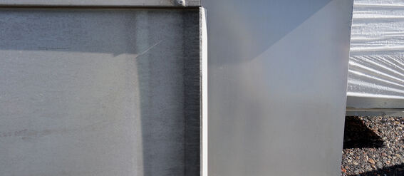 Two large aluminum sheets leaning against each other on a gravel surface with a white tarp in the background.
