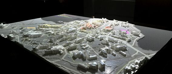 A detailed architectural model of a city displayed on a table in a dimly lit room.