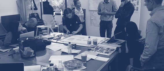 A group of people in a meeting room with laptops, papers, and drinks on the table, discussing and collaborating.