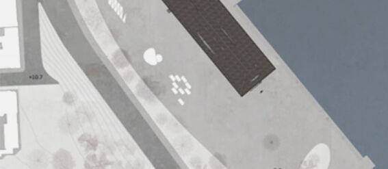 Aerial view of a waterfront area with a rectangular building, pathways, and scattered trees.