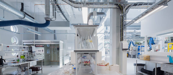 A modern laboratory with equipment, shelves, and tables. Ventilation ducts are visible on the ceiling.