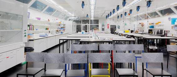 A modern laboratory with workstations and colourful chairs. Shelves with equipment line the walls. Large windows provide natural light.