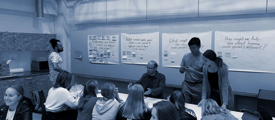 A group of people in a classroom discussing ideas written on large papers on the wall.