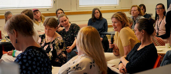Group of adults seated in a bright meeting room, one person holding a microphone to speak
