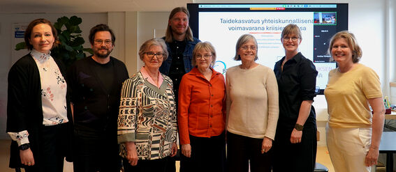 Group of adults posing indoors in front of a large presentation screen 