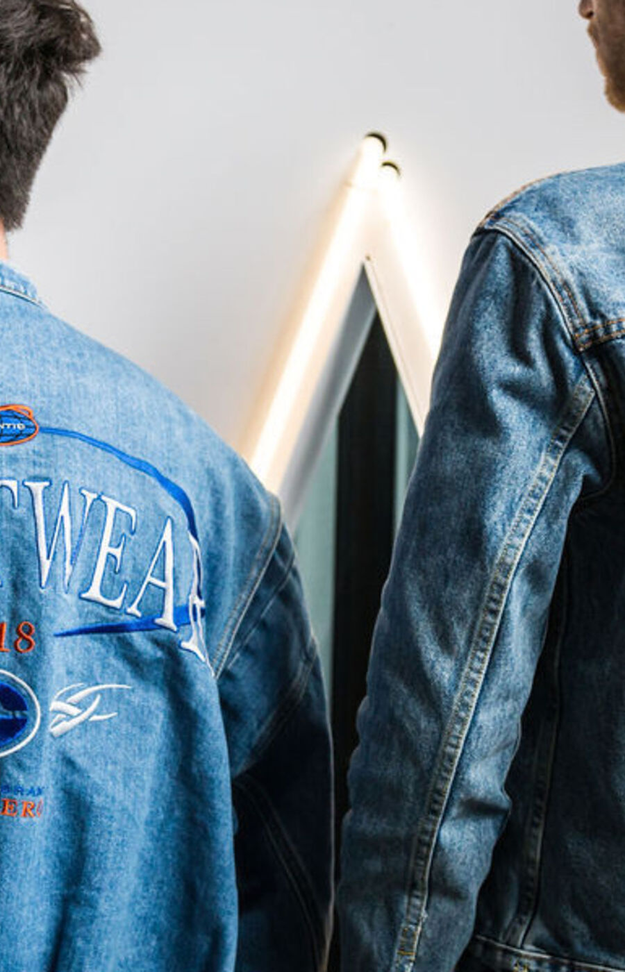 kaksi farkkutakkista miestä esittelee kirjailtuja takinselkiään selin kameraan