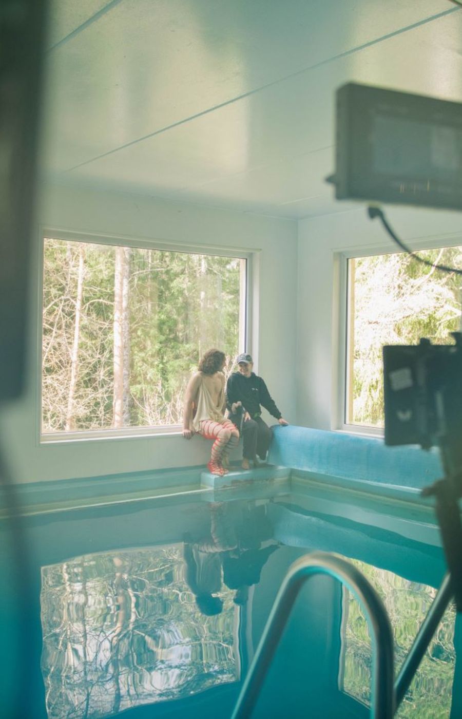 Two people sitting by a pool, with camera filming them