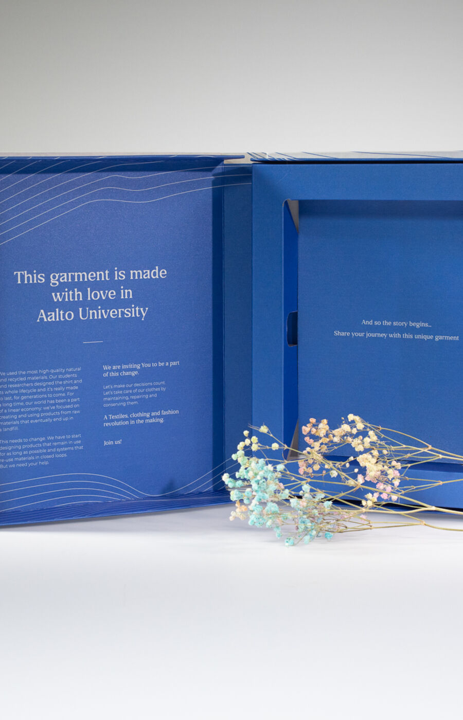 Open blue box with text from Aalto University and a sprig of delicate flowers on a white surface.