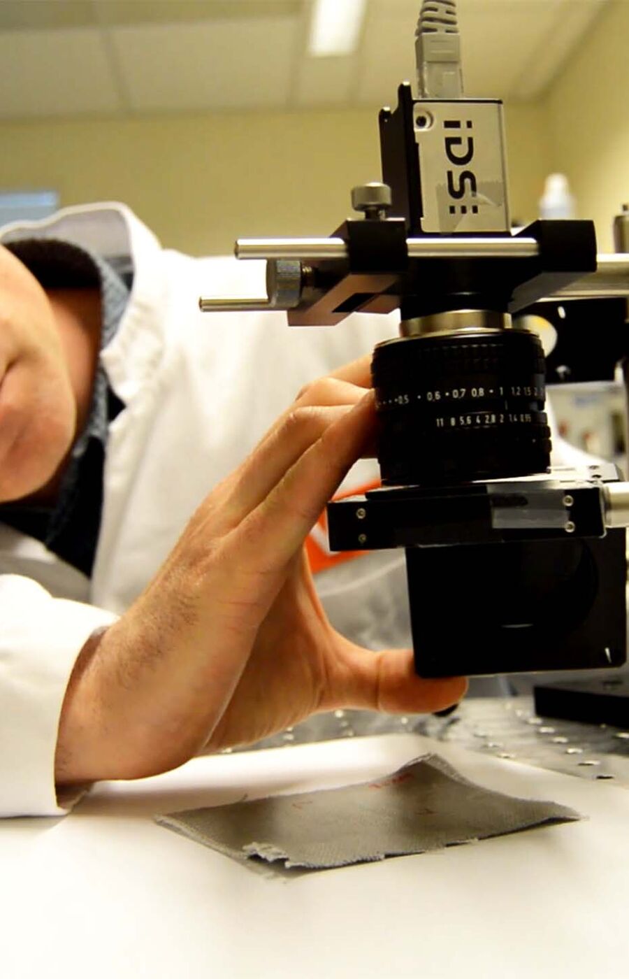 A scientist in a white lab coat and protective glasses adjusts equipment in a laboratory.
