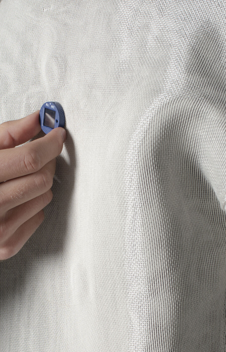 A hand in a patterned sleeve holds a small blue object against a light grey fabric.