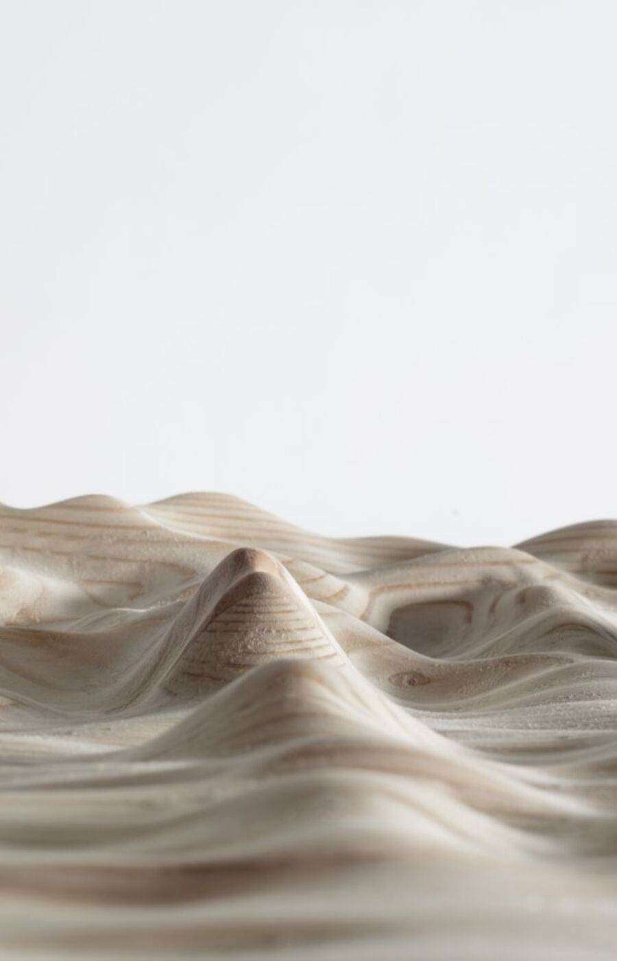 A close-up of a wooden surface carved to resemble a mountainous landscape with smooth peaks and valleys.