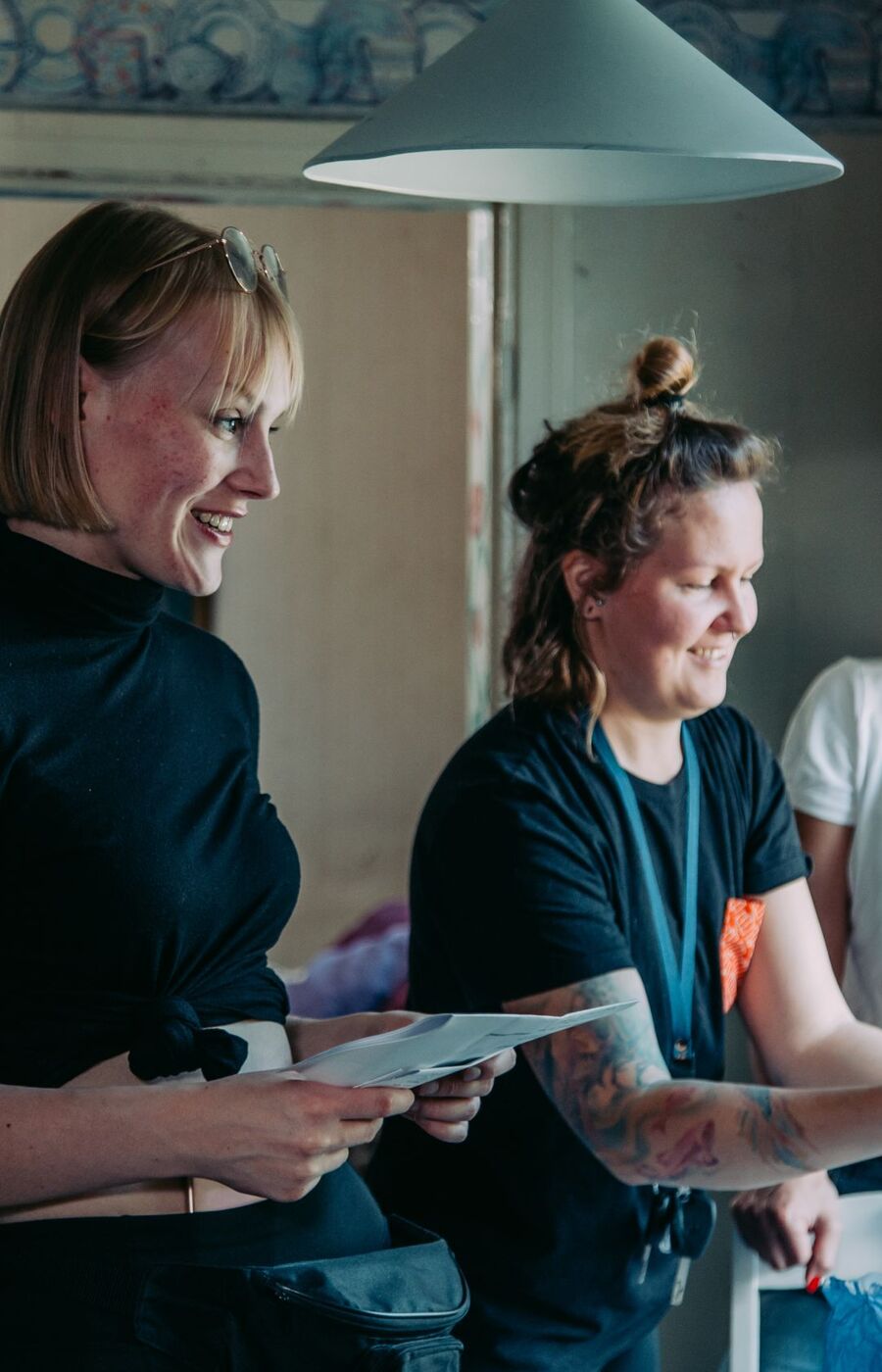 Three people in a kitchen, one holding a cake, another holding papers. The kitchen has a vintage look with a teal cabinet.