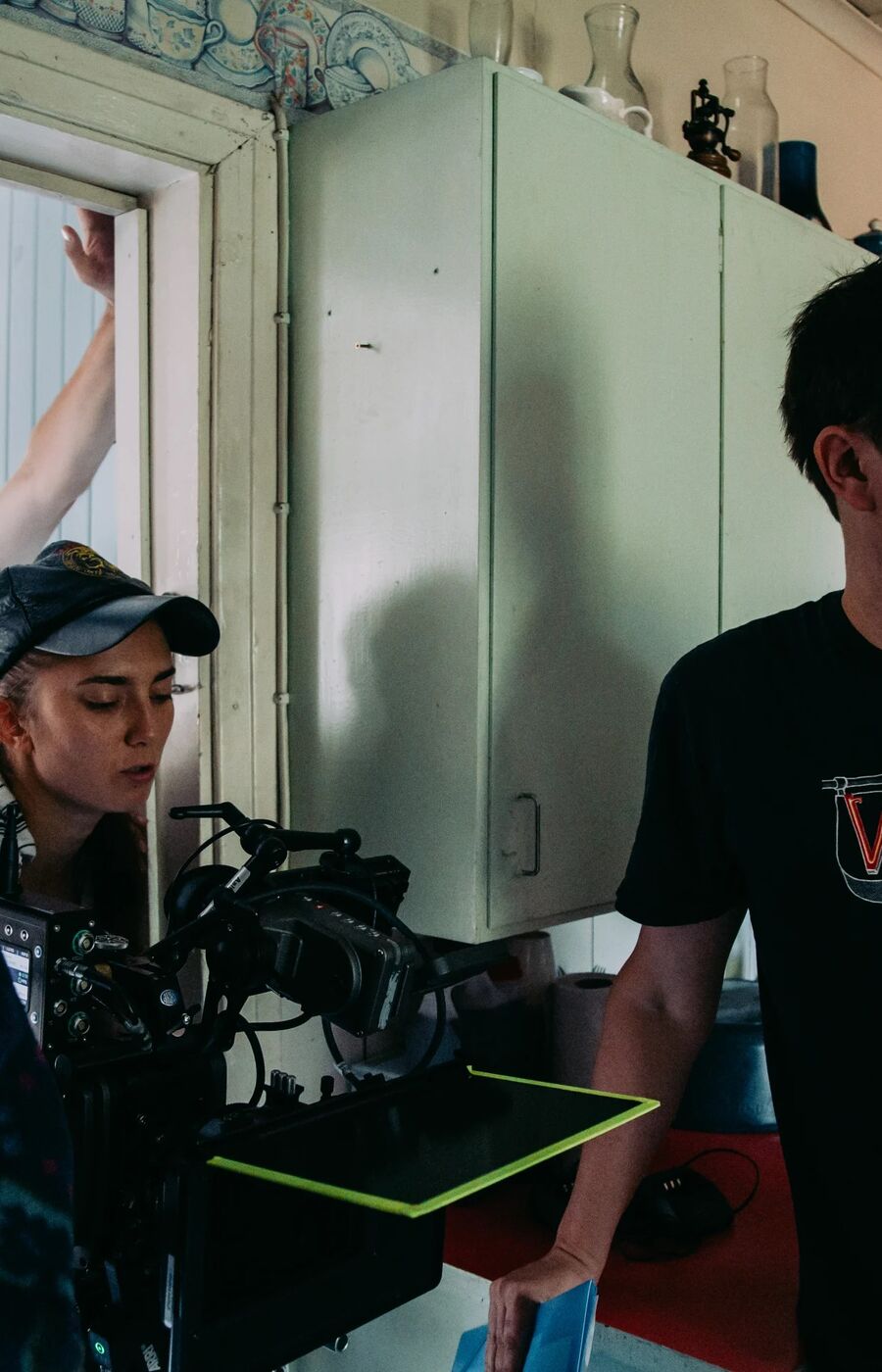 Several people are in a room with filming equipment. One person wears a black 'Village Vanguard' T-shirt.