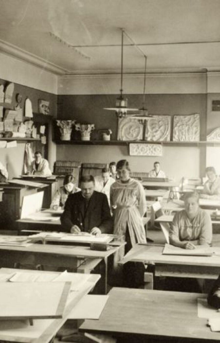A vintage classroom with students working at drafting tables, surrounded by architectural drawings and models.