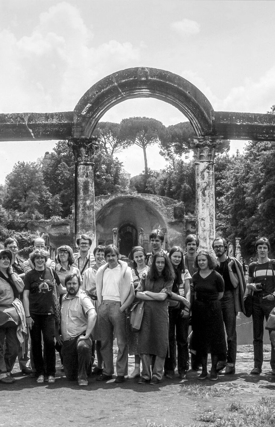 A group of people standing in front of ancient Roman ruins with arches and statues.