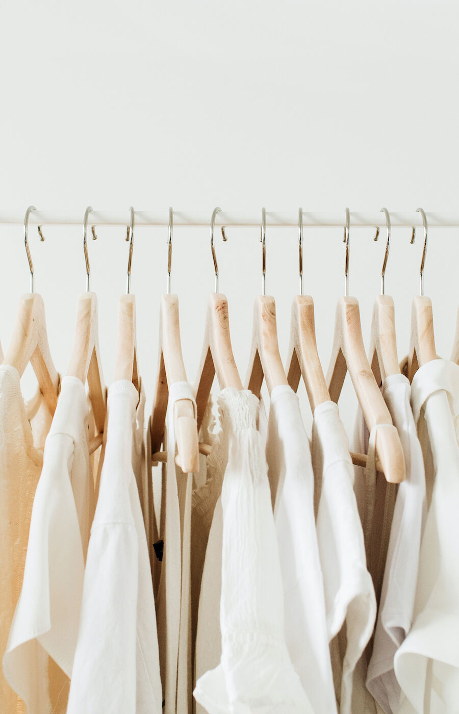 A row of white and beige clothes on wooden hangers on a white clothing rack.