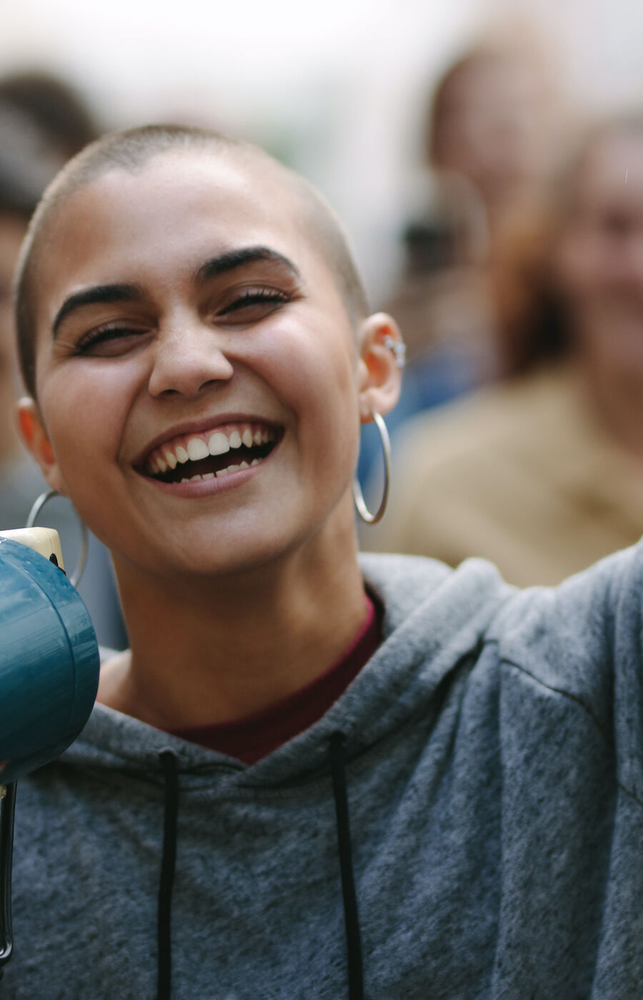 A person in a grey hoodie holds a megaphone, surrounded by a crowd.
