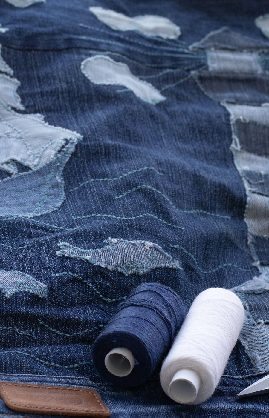 Denim jacket with embroidered ship and lighthouse, surrounded by clouds. Threads and scissors are placed on the jacket.