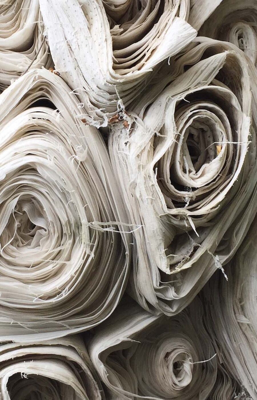 Close-up of several rolls of beige fabric stacked together, showing frayed edges and intricate folds.