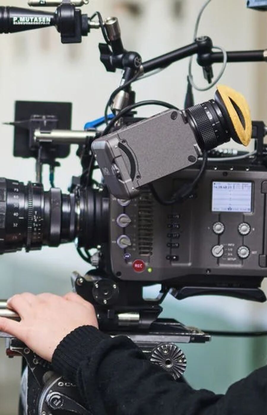 A person operating a professional ARRI video camera with various attachments indoors.