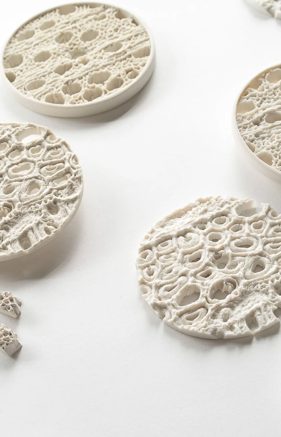 Useita pyöreitä, valkoisia esineitä, joissa on monimutkaisia pitsimäisiä kuvioita, on hajallaan valkoisella pinnalla.