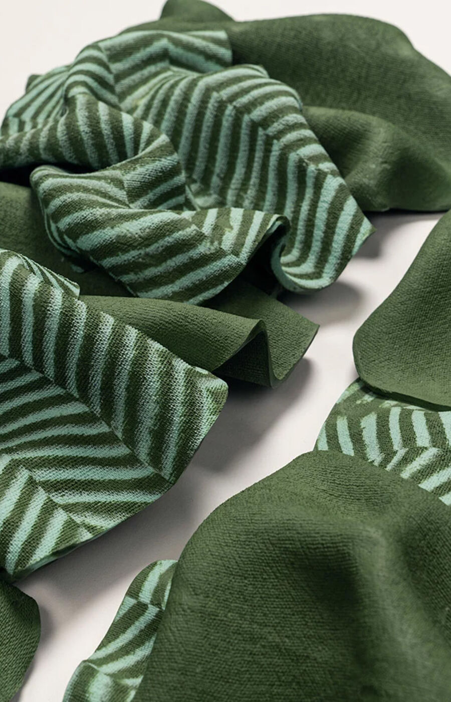 Vihreä kangas, jossa vaaleanvihreät siksak-kuviot, ryppyinen ja levitetty valkoiselle pinnalle.