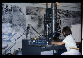 Historiallisessa arkistokuvassa valkoiseen työtakkiin pukeutunut nainen ohjaa suurikokoista kuvantamaislaitetta.