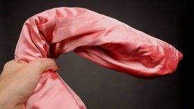 kuva pitkulalle rullatusta vaalenpunaisesta satiinikankaasta ja kädestä joka pitelee sitä. Tumma tausta.