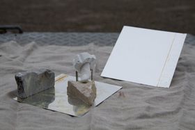 Kankaan päällä asetelma kiviä ja kaksi jonkinlaista heijastavaa, melkein peilinomaista neliönmallista peltiä